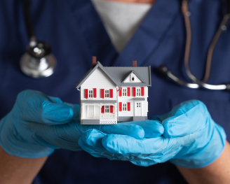 a miniature house in glove hands of a medical staff member